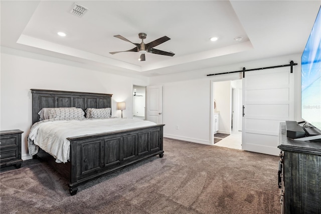 carpeted bedroom featuring a barn door, ceiling fan, connected bathroom, and a tray ceiling