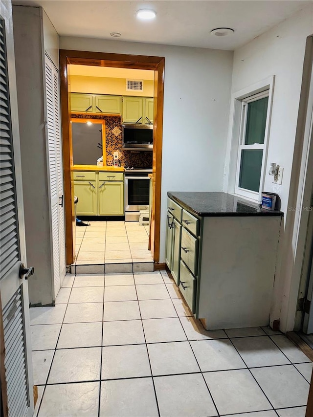 kitchen featuring green cabinets, decorative backsplash, stainless steel appliances, and light tile patterned flooring