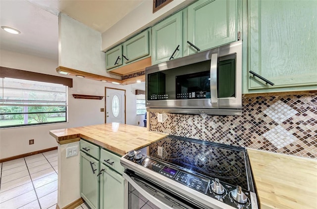 kitchen with light tile patterned floors, butcher block counters, backsplash, stainless steel appliances, and green cabinetry