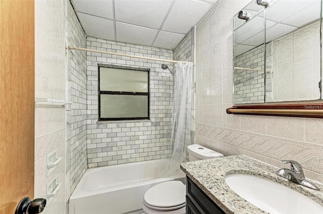 full bathroom with toilet, tile walls, vanity, shower / bath combo with shower curtain, and a drop ceiling