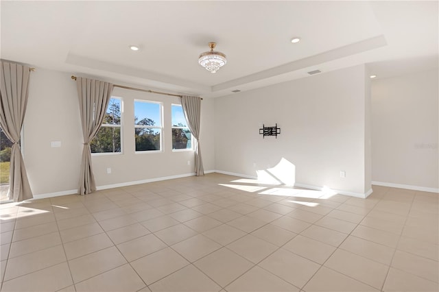 spare room featuring a raised ceiling and light tile patterned flooring