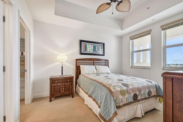 bedroom featuring ceiling fan, a tray ceiling, and light carpet