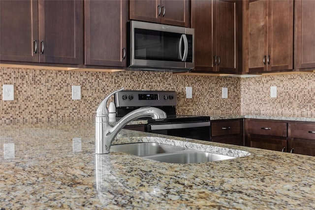 kitchen with dark brown cabinetry, sink, tasteful backsplash, appliances with stainless steel finishes, and light stone countertops