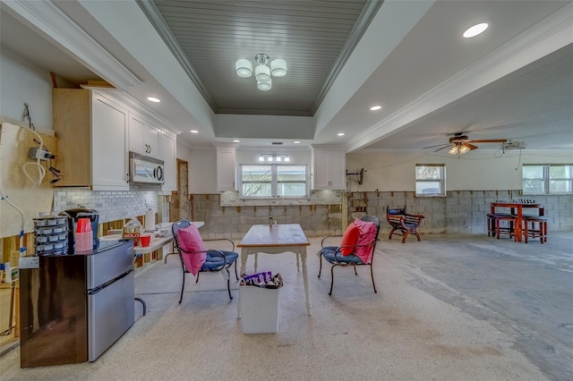 kitchen with white cabinetry, ornamental molding, a tray ceiling, stainless steel appliances, and backsplash