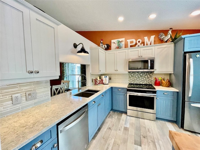 kitchen with appliances with stainless steel finishes, blue cabinets, sink, white cabinets, and light wood-type flooring