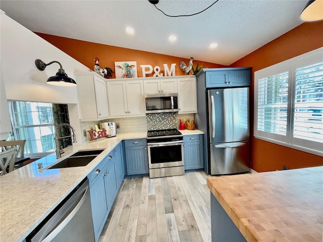 kitchen with lofted ceiling, sink, appliances with stainless steel finishes, butcher block counters, and white cabinets