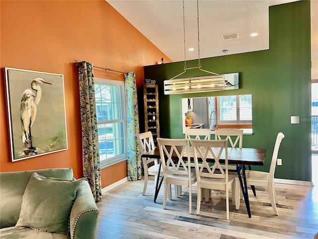 dining space with lofted ceiling, a textured ceiling, and light wood-type flooring