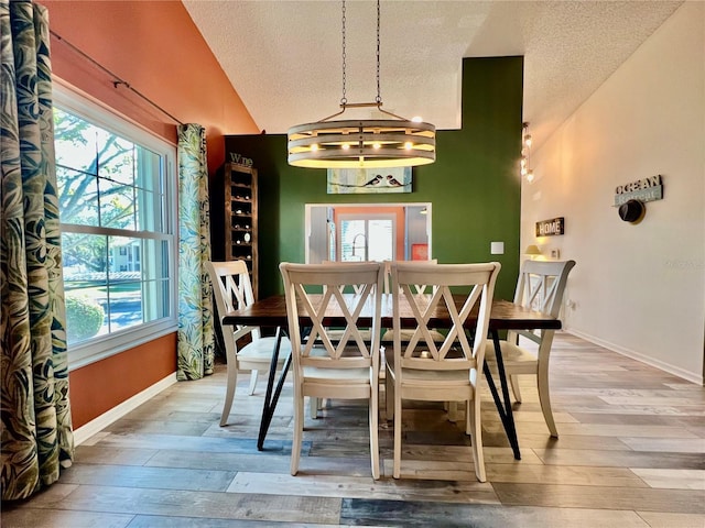 dining room with hardwood / wood-style flooring, vaulted ceiling, and a textured ceiling