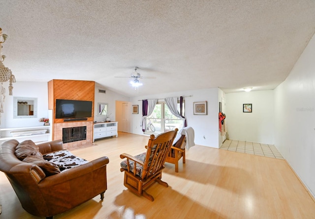 living room featuring a fireplace, lofted ceiling, light hardwood / wood-style floors, ceiling fan, and a textured ceiling