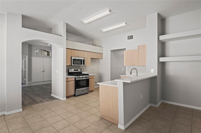 kitchen with light tile patterned floors, sink, stainless steel appliances, light brown cabinetry, and kitchen peninsula