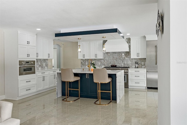 kitchen featuring stainless steel appliances, decorative light fixtures, a center island with sink, and white cabinets