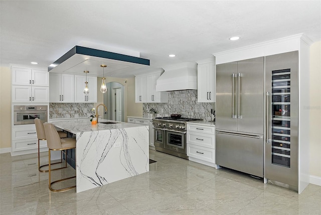 kitchen featuring white cabinetry, high end appliances, custom range hood, and a kitchen island with sink