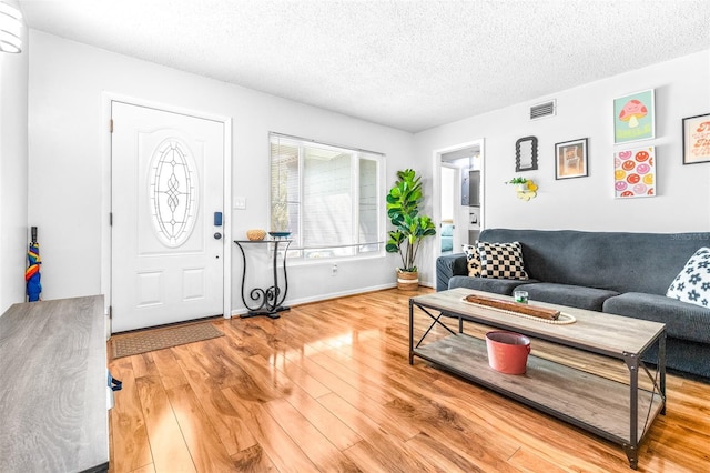 living area with visible vents, a textured ceiling, baseboards, and wood finished floors