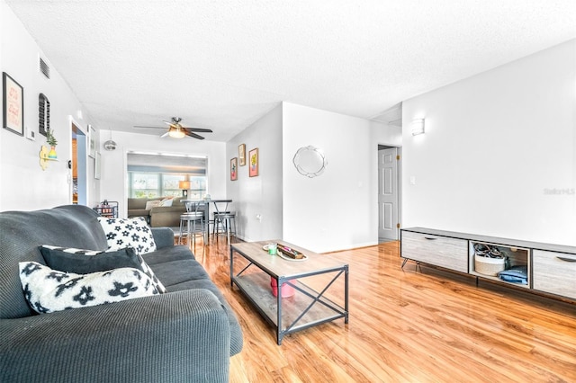 living area featuring ceiling fan, a textured ceiling, visible vents, and wood finished floors