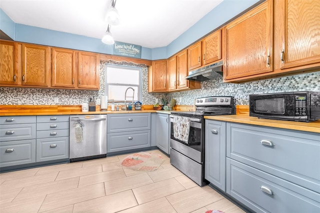 kitchen featuring decorative backsplash, appliances with stainless steel finishes, brown cabinetry, a sink, and under cabinet range hood