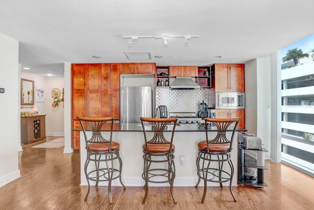 kitchen featuring a breakfast bar area, appliances with stainless steel finishes, backsplash, track lighting, and light hardwood / wood-style floors