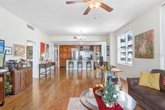 living room featuring ceiling fan with notable chandelier and light hardwood / wood-style flooring