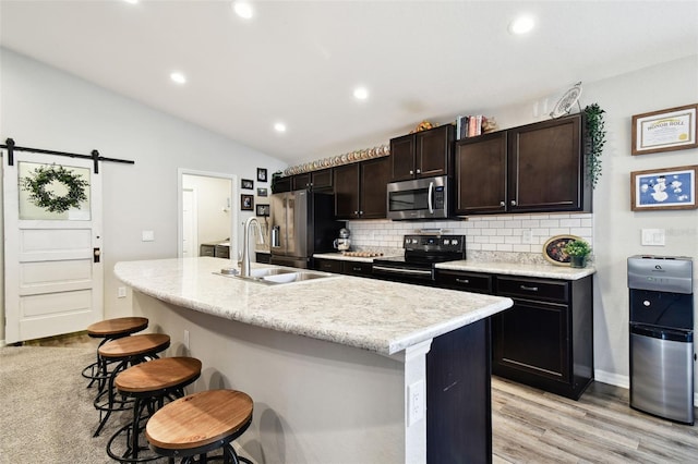 kitchen with sink, a kitchen breakfast bar, stainless steel appliances, a barn door, and a center island with sink