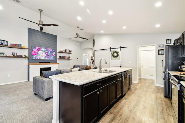 kitchen with lofted ceiling, sink, appliances with stainless steel finishes, an island with sink, and a barn door