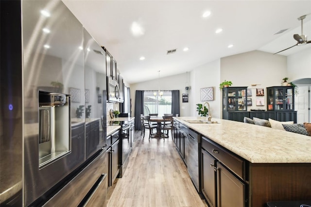 kitchen with stainless steel appliances, vaulted ceiling, sink, and a center island with sink