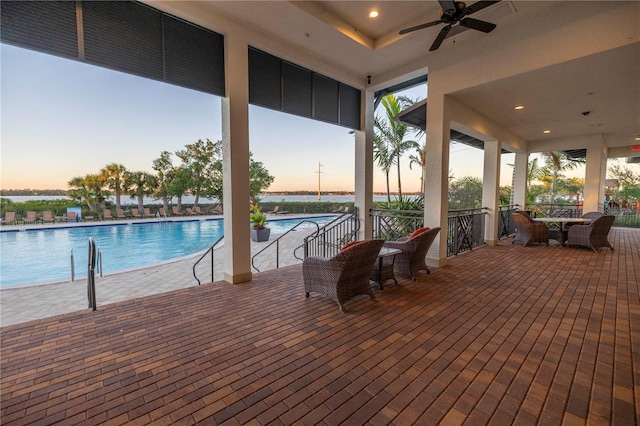 pool at dusk with ceiling fan and a patio area