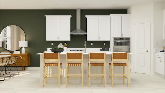 kitchen featuring wall chimney range hood, a kitchen bar, and white cabinets