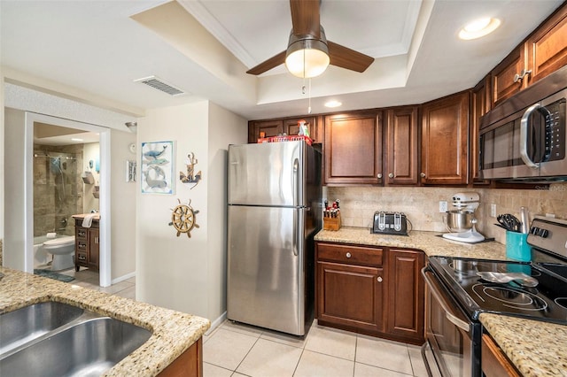 kitchen with tasteful backsplash, stainless steel appliances, a raised ceiling, and light stone countertops