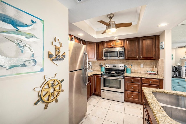 kitchen featuring stainless steel appliances, tasteful backsplash, light stone counters, and a tray ceiling