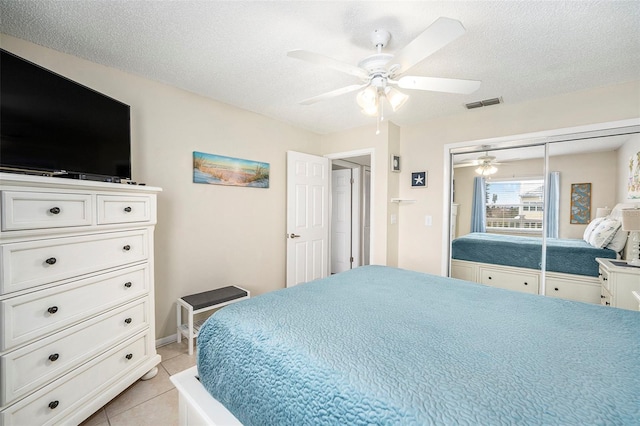 bedroom featuring ceiling fan, a closet, a textured ceiling, and light tile patterned flooring