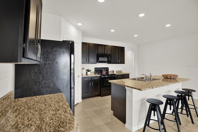 kitchen featuring a breakfast bar, sink, light stone counters, a kitchen island with sink, and black appliances