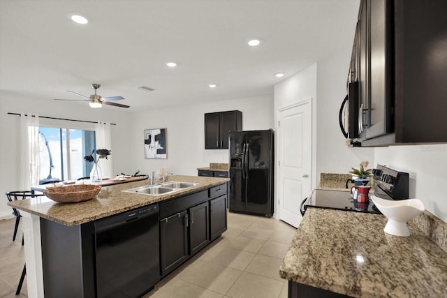 kitchen with light stone countertops, sink, a center island with sink, and black appliances