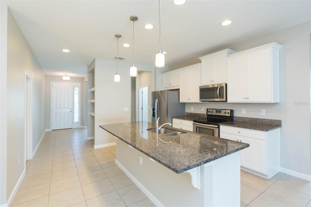 kitchen featuring stainless steel appliances, white cabinets, decorative light fixtures, and an island with sink