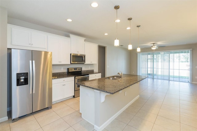 kitchen with a sink, white cabinets, appliances with stainless steel finishes, dark stone counters, and a center island with sink