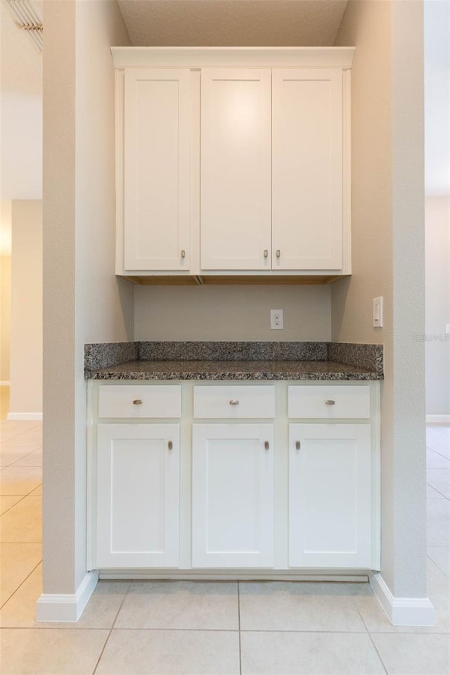 kitchen featuring baseboards, white cabinetry, dark stone countertops, and light tile patterned floors