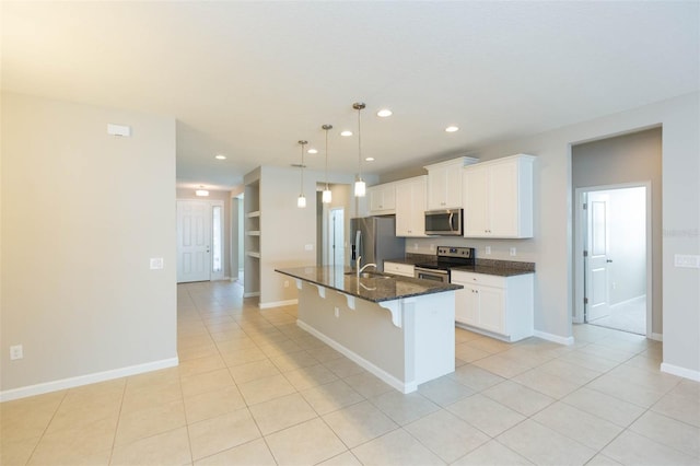 kitchen featuring white cabinets, an island with sink, a kitchen breakfast bar, dark stone countertops, and stainless steel appliances