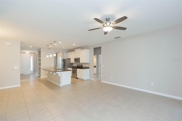 kitchen with dark countertops, an island with sink, appliances with stainless steel finishes, white cabinetry, and pendant lighting