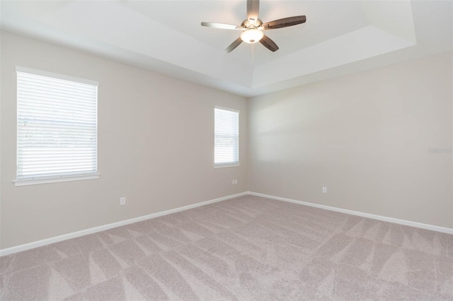 unfurnished room with baseboards, ceiling fan, a tray ceiling, and light colored carpet