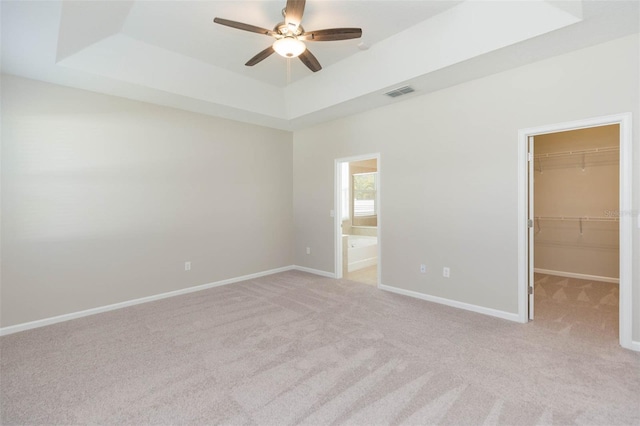 unfurnished bedroom featuring baseboards, visible vents, a raised ceiling, light colored carpet, and a walk in closet