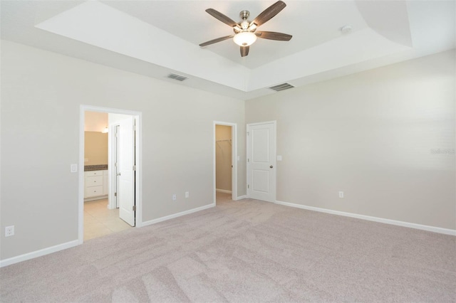 unfurnished bedroom with light colored carpet, a tray ceiling, a walk in closet, and visible vents