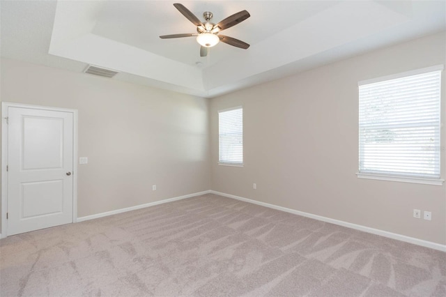 spare room with baseboards, visible vents, a raised ceiling, light colored carpet, and ceiling fan