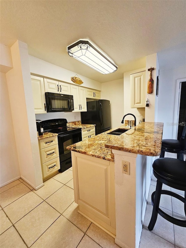 kitchen with black appliances, sink, light tile patterned floors, light stone counters, and kitchen peninsula