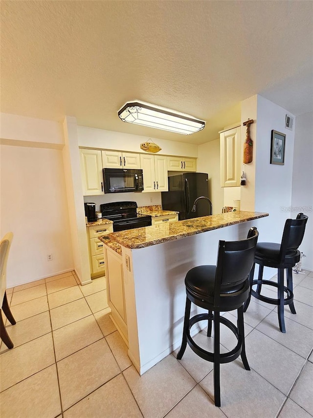 kitchen featuring black appliances, dark stone countertops, a breakfast bar area, light tile patterned floors, and kitchen peninsula