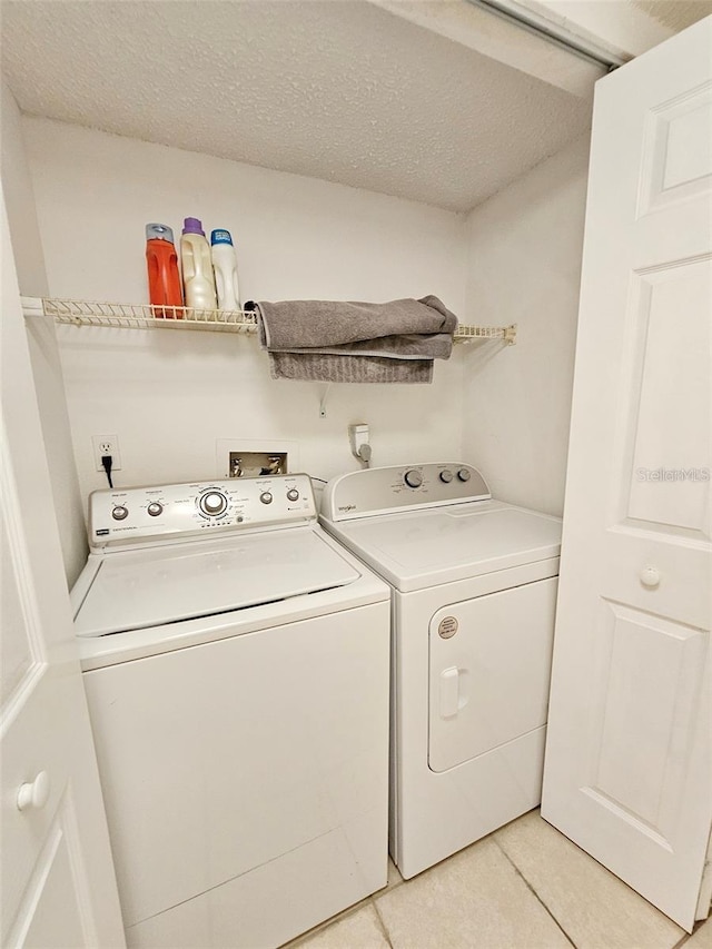 laundry area featuring light tile patterned floors, a textured ceiling, and washer and clothes dryer