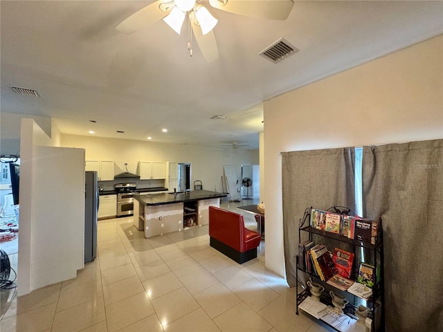 kitchen featuring light tile patterned flooring, appliances with stainless steel finishes, white cabinetry, a kitchen island with sink, and ceiling fan