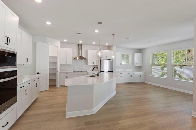 kitchen featuring visible vents, light wood-style flooring, stainless steel appliances, wall chimney range hood, and tasteful backsplash