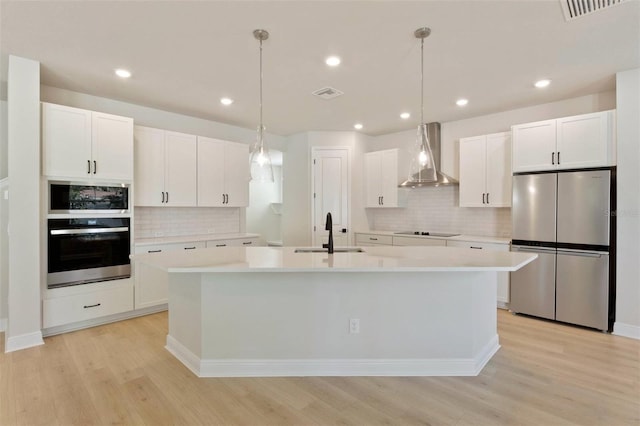 kitchen with visible vents, a sink, freestanding refrigerator, wall chimney range hood, and black electric cooktop