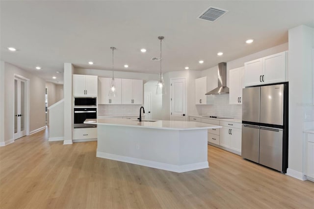 kitchen featuring visible vents, wall chimney range hood, appliances with stainless steel finishes, white cabinets, and a sink