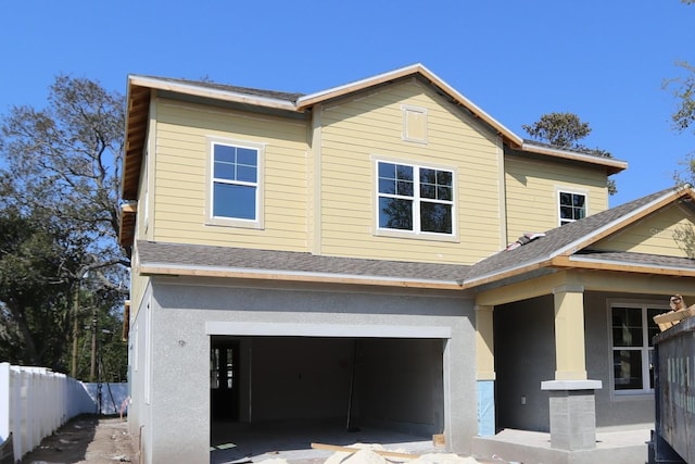 view of front of property with a garage, a shingled roof, stucco siding, and fence