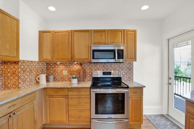 kitchen with light stone counters, decorative backsplash, stainless steel appliances, and light hardwood / wood-style floors