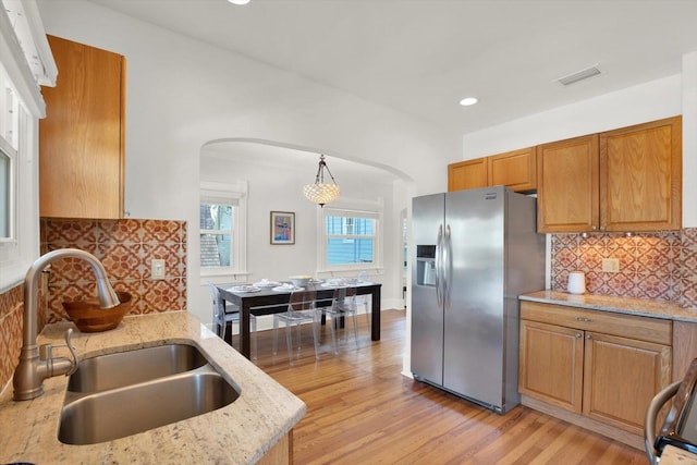 kitchen featuring pendant lighting, sink, light hardwood / wood-style flooring, light stone countertops, and stainless steel fridge with ice dispenser